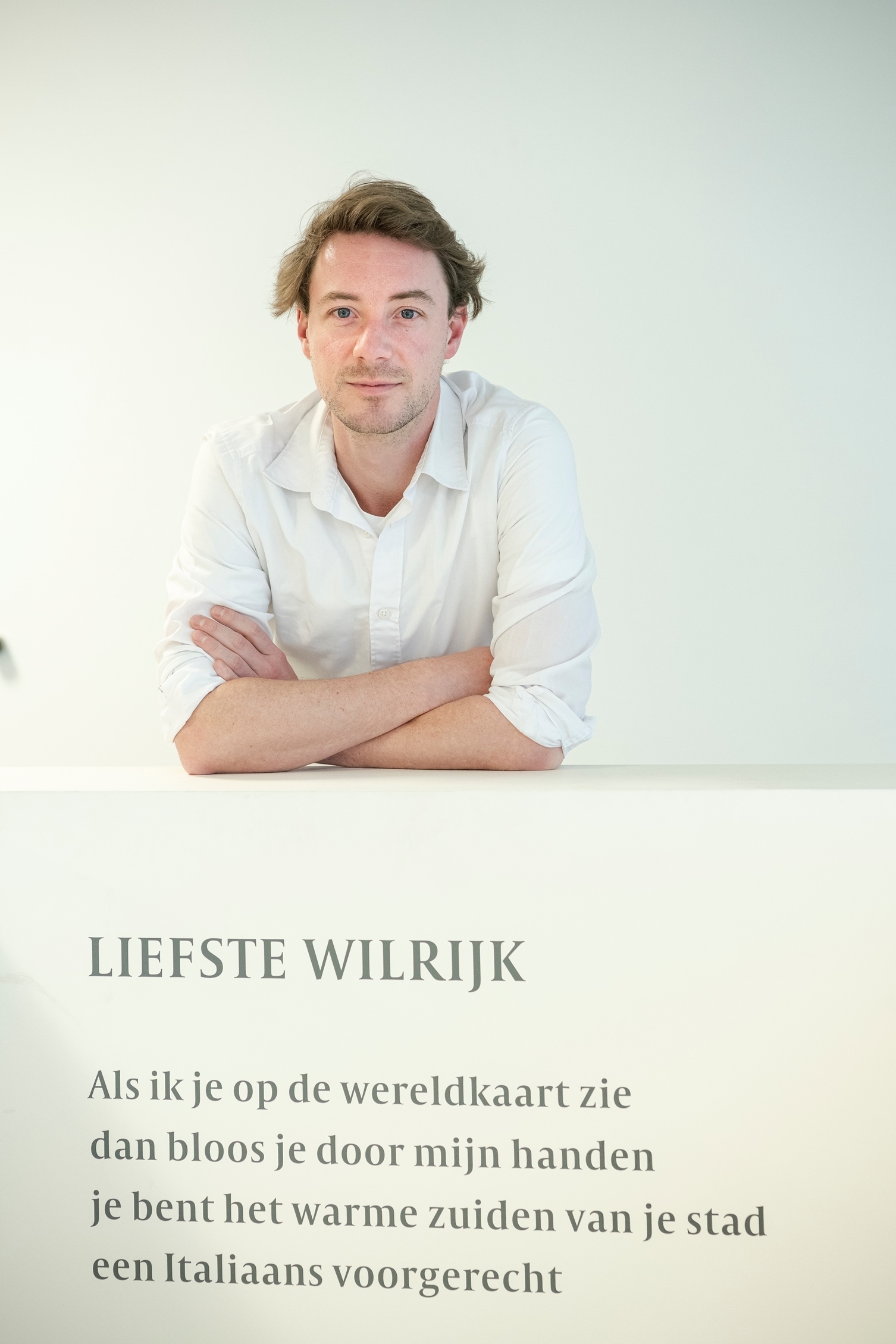 De dichter poseert bij een muur waarop een stuk tekst van het gedicht staat. De dichter poseert bij een muur waarop een stuk tekst van het gedicht staat.